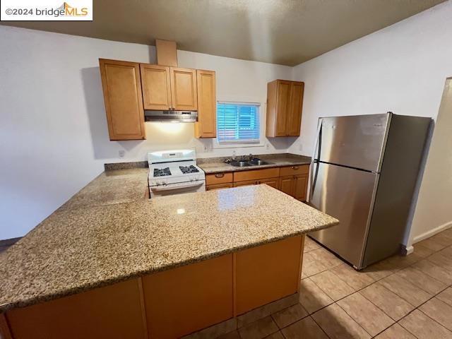 kitchen with stainless steel refrigerator, light stone countertops, white range with gas stovetop, kitchen peninsula, and light tile patterned floors