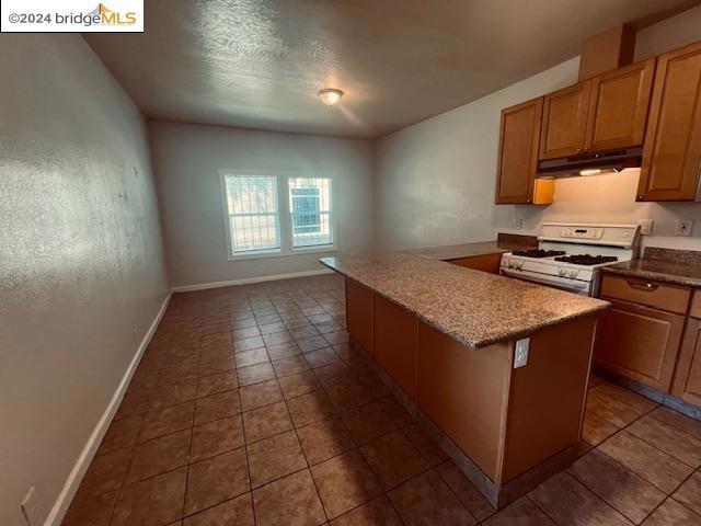 kitchen with a center island, light tile patterned flooring, light stone countertops, and white range with gas cooktop