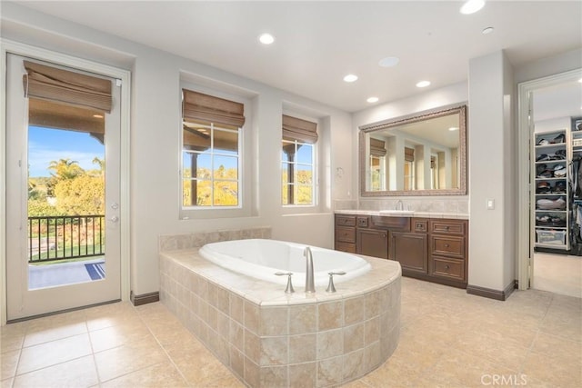 bathroom with a relaxing tiled tub, vanity, and tile patterned flooring