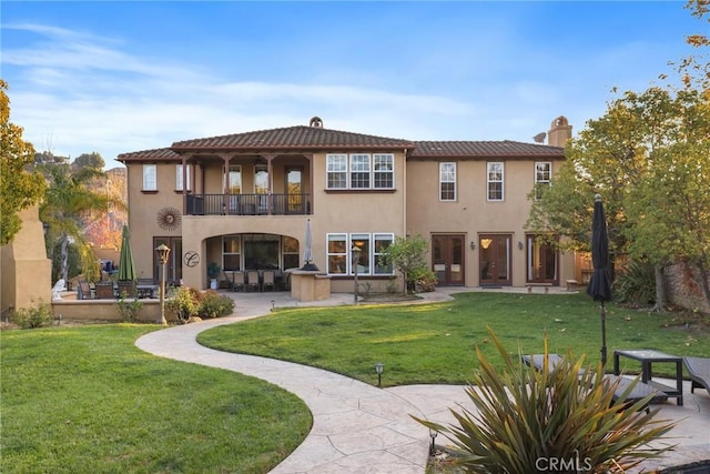 rear view of property with a balcony, stucco siding, a lawn, and a patio