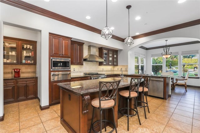 kitchen with a center island with sink, glass insert cabinets, stainless steel appliances, wall chimney range hood, and a warming drawer