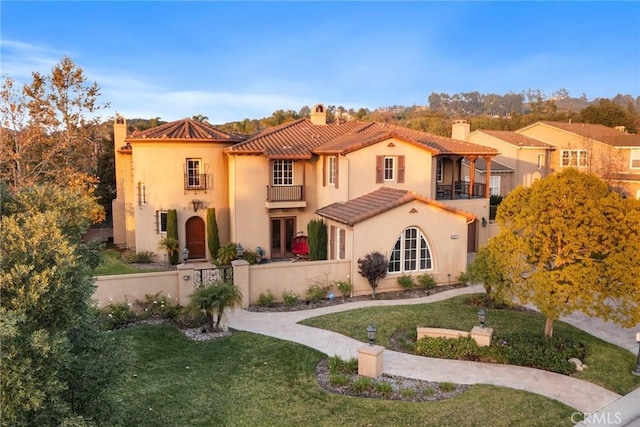 mediterranean / spanish-style home featuring a front lawn and a balcony