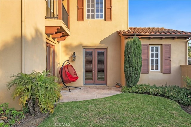 property entrance featuring a patio, a lawn, a tile roof, and stucco siding