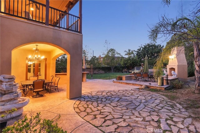 patio terrace at dusk featuring an outdoor fireplace and a balcony