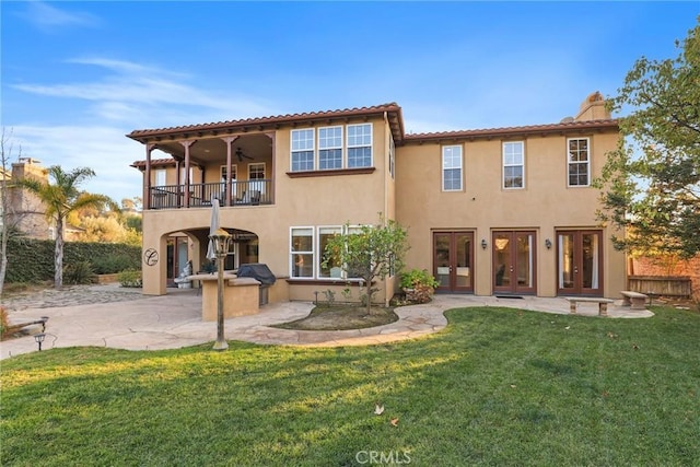 rear view of house featuring a balcony, a patio area, a lawn, and french doors