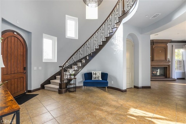 tiled entrance foyer with arched walkways, a towering ceiling, visible vents, baseboards, and stairway