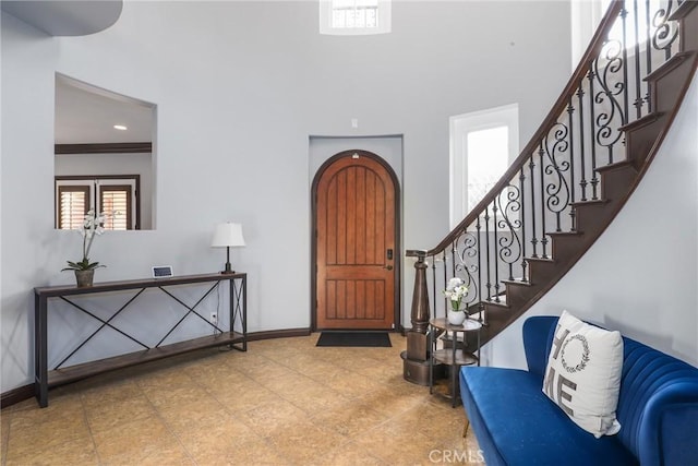 entrance foyer featuring a towering ceiling, arched walkways, stairway, and baseboards