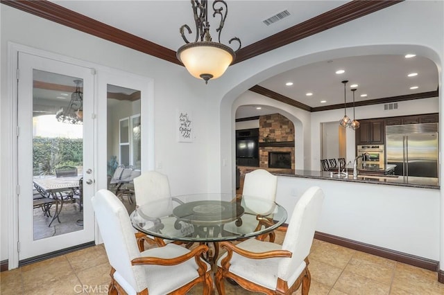 dining space with sink, ornamental molding, a stone fireplace, and light tile patterned flooring