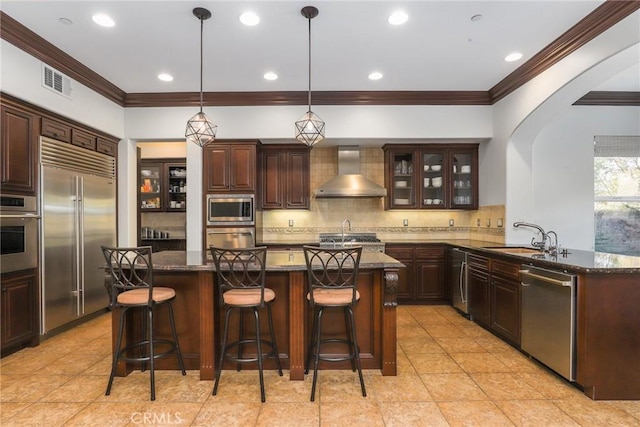 kitchen with wall chimney range hood, kitchen peninsula, a kitchen bar, sink, and built in appliances