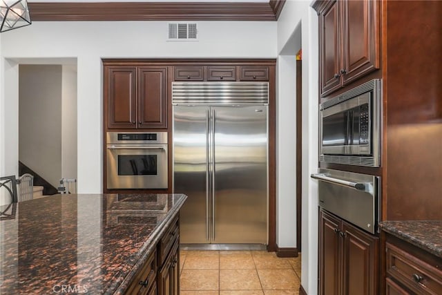 kitchen featuring visible vents, dark stone counters, ornamental molding, built in appliances, and a warming drawer