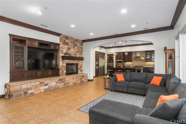 living area featuring arched walkways, a stone fireplace, recessed lighting, baseboards, and ornamental molding