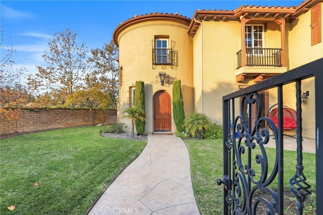 mediterranean / spanish house featuring a tiled roof, a front yard, fence, and stucco siding