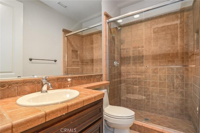 bathroom featuring toilet, tasteful backsplash, a shower with door, and vanity