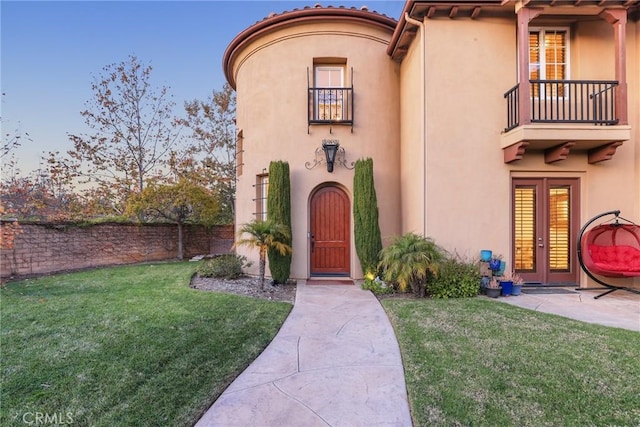 exterior entry at dusk with a balcony, a lawn, and french doors