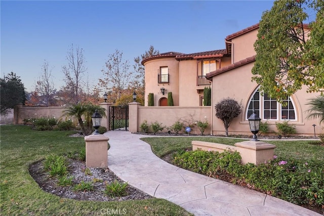 view of front of house featuring a fenced front yard, a balcony, a tiled roof, stucco siding, and a front lawn