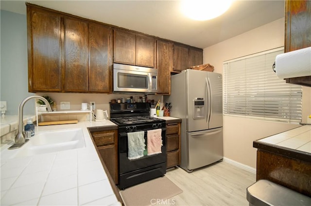 kitchen featuring tile counters, sink, stainless steel appliances, and light hardwood / wood-style flooring