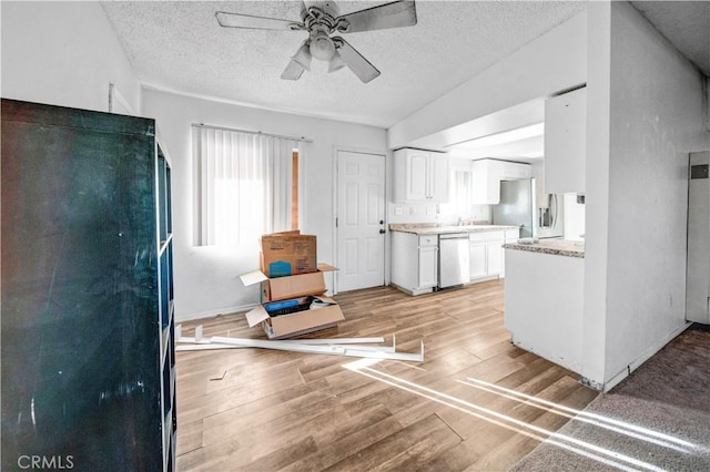 kitchen featuring vaulted ceiling, light wood-type flooring, a textured ceiling, appliances with stainless steel finishes, and white cabinetry