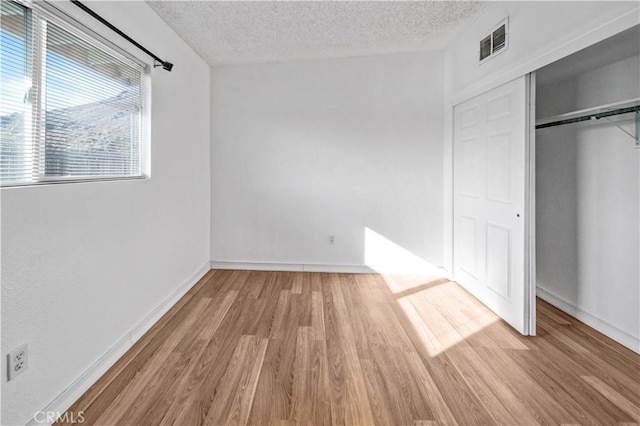 unfurnished bedroom featuring light hardwood / wood-style floors, a textured ceiling, and a closet