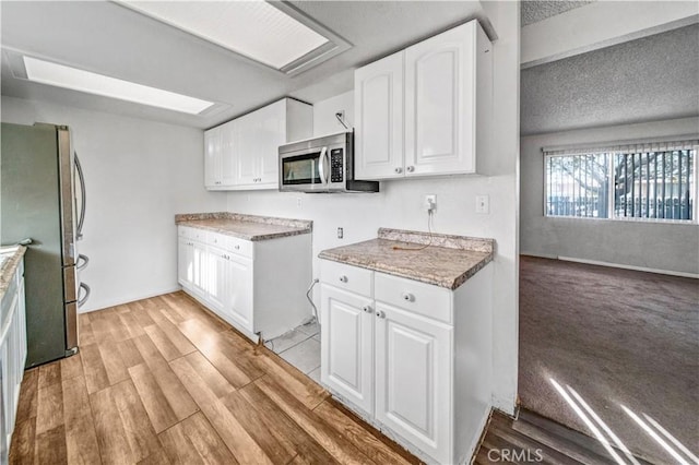 kitchen with light wood-type flooring, a textured ceiling, stainless steel appliances, beam ceiling, and white cabinetry