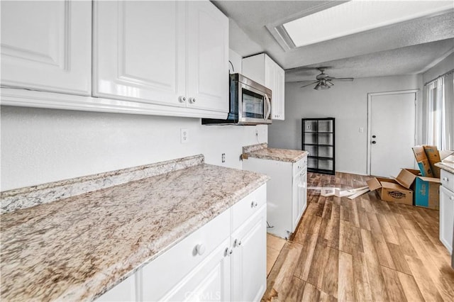 kitchen featuring light stone countertops, light wood-type flooring, a textured ceiling, ceiling fan, and white cabinetry