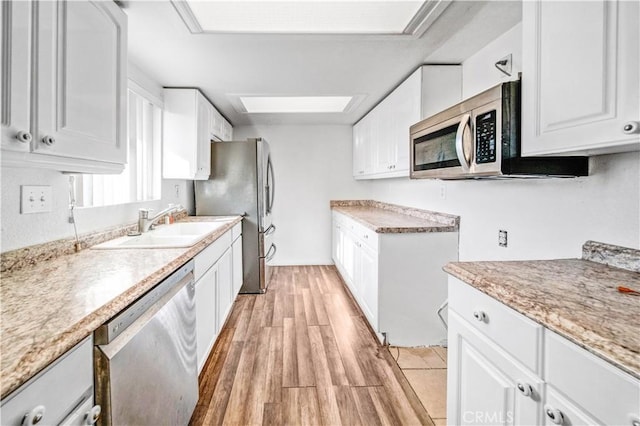 kitchen featuring white cabinets, sink, a skylight, appliances with stainless steel finishes, and light hardwood / wood-style floors