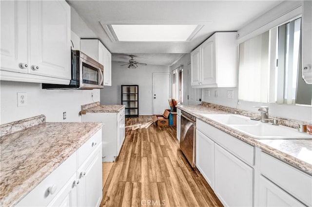 kitchen with sink, a skylight, light wood-type flooring, white cabinetry, and stainless steel appliances