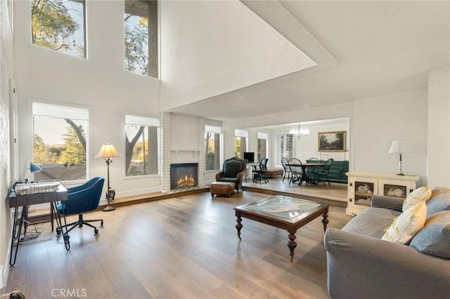 living room featuring hardwood / wood-style flooring, a towering ceiling, a fireplace, and a notable chandelier