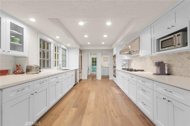 kitchen featuring white cabinetry, stainless steel appliances, wall chimney exhaust hood, and light wood-type flooring