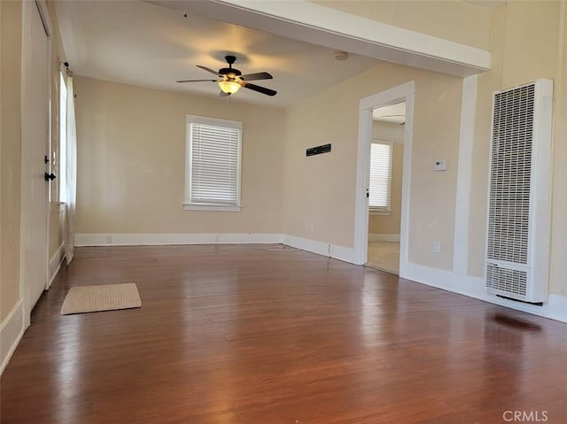 empty room with baseboards, wood finished floors, a heating unit, and ceiling fan