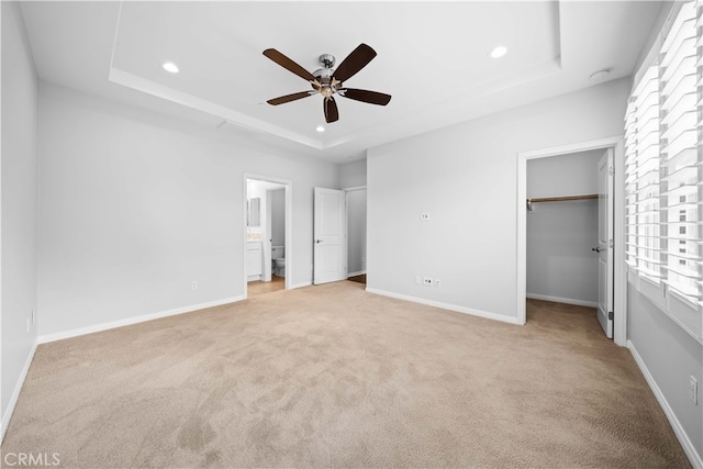 unfurnished bedroom with light carpet, ensuite bath, a raised ceiling, ceiling fan, and a closet