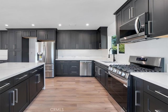 kitchen featuring light stone countertops, sink, stainless steel appliances, and light hardwood / wood-style flooring