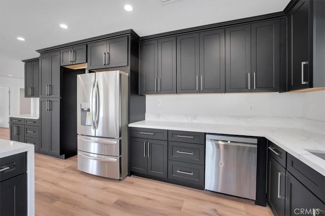 kitchen with light wood-type flooring, appliances with stainless steel finishes, and light stone countertops