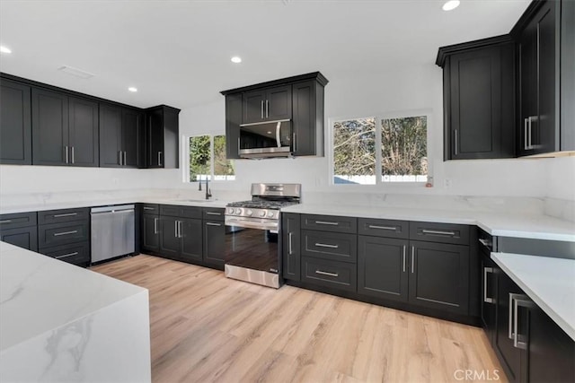 kitchen featuring light stone countertops, appliances with stainless steel finishes, light hardwood / wood-style flooring, and sink