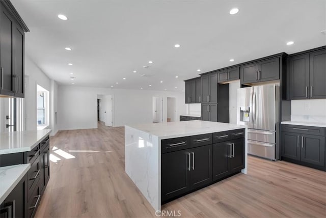 kitchen featuring stainless steel refrigerator with ice dispenser, light hardwood / wood-style flooring, a center island, and light stone countertops