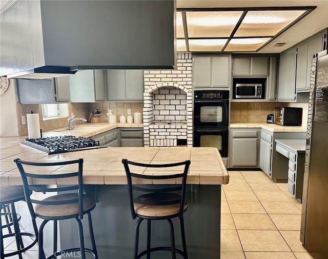 kitchen with a kitchen bar, gray cabinetry, light tile patterned floors, kitchen peninsula, and stainless steel appliances