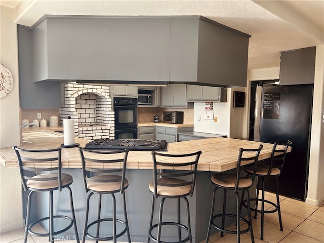 kitchen with appliances with stainless steel finishes, kitchen peninsula, decorative backsplash, and gray cabinetry