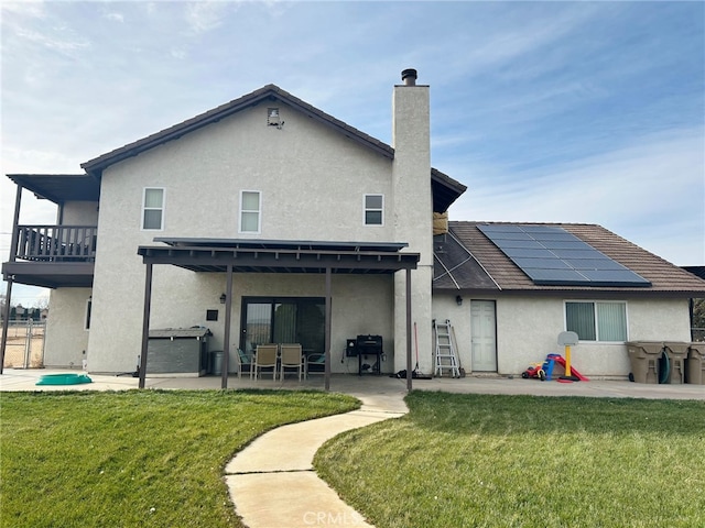 back of property with solar panels, a balcony, a lawn, a jacuzzi, and a patio area