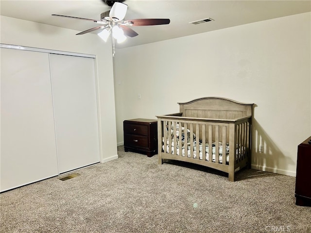 bedroom with a nursery area, a closet, ceiling fan, and light carpet