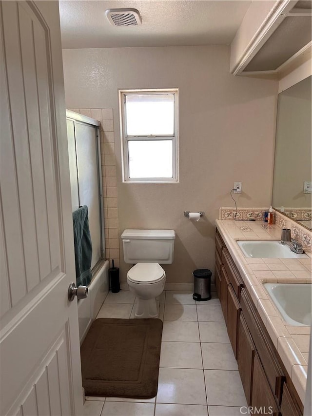 full bathroom featuring bath / shower combo with glass door, tile patterned flooring, vanity, toilet, and a textured ceiling