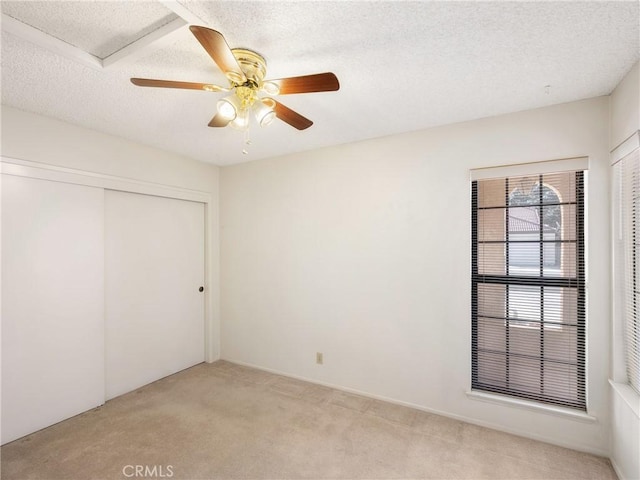 unfurnished bedroom with ceiling fan, light colored carpet, a textured ceiling, and a closet