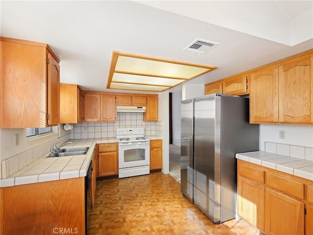 kitchen with tile counters, white electric range, sink, and stainless steel refrigerator