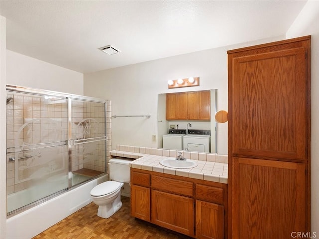 full bathroom featuring combined bath / shower with glass door, parquet floors, vanity, independent washer and dryer, and toilet