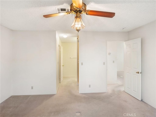 unfurnished room with a textured ceiling, light colored carpet, and ceiling fan