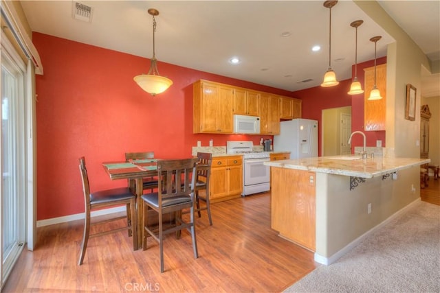 kitchen with white appliances, a kitchen breakfast bar, sink, decorative light fixtures, and kitchen peninsula