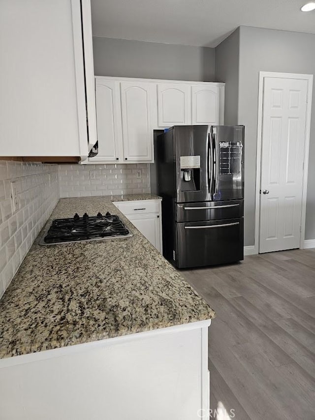 kitchen with decorative backsplash, light wood-type flooring, light stone counters, white cabinetry, and stainless steel appliances