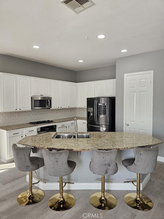 kitchen featuring a breakfast bar, sink, an island with sink, appliances with stainless steel finishes, and white cabinetry