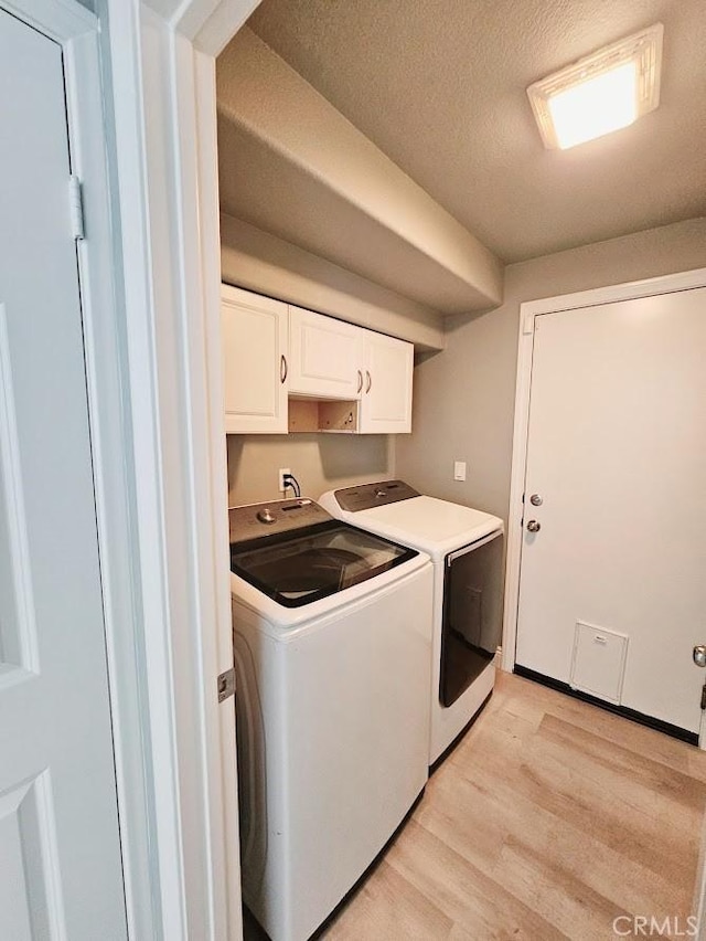 laundry area featuring washing machine and dryer, cabinets, a textured ceiling, and light wood-type flooring