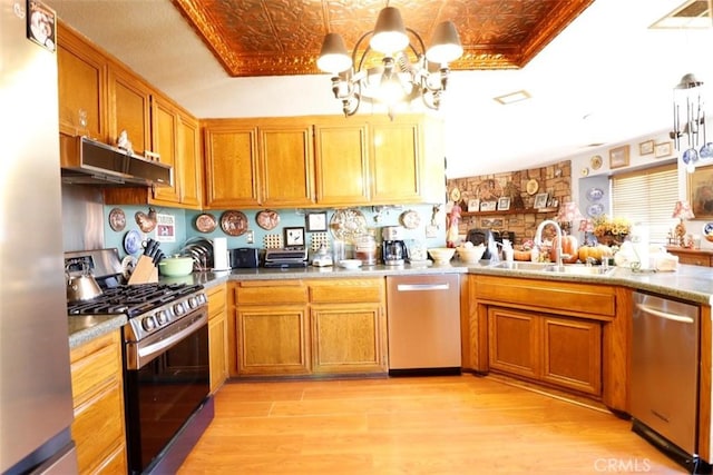 kitchen featuring appliances with stainless steel finishes, light wood-type flooring, decorative light fixtures, and sink