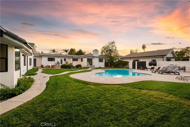 pool at dusk with a yard and a patio