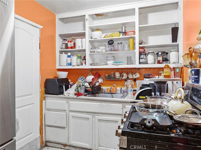 kitchen with stainless steel fridge, white cabinetry, and sink